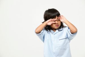 Young child rubbing his eyes, showing signs of possible eye discomfort or vision issues.
