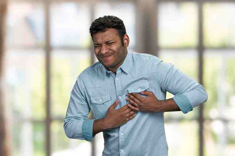 Young man clutching his chest in pain, indicating a possible heart attack.