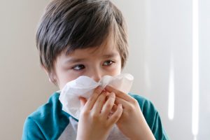 A young kid is blowing his nose with a tissue, showing common cold and fever symptoms.