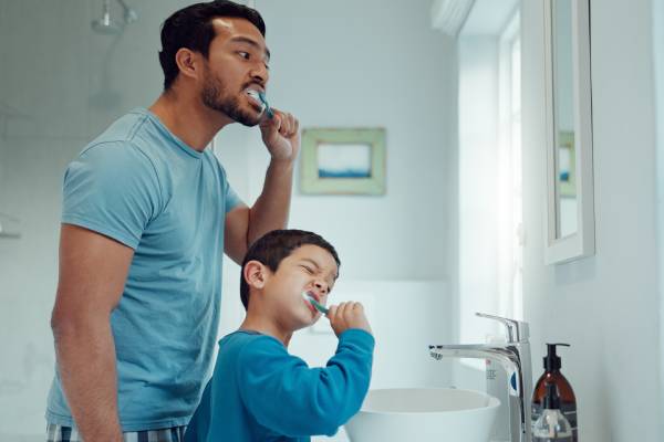 Father and son brushing their teeth, showing how playful routines can encourage kids to brush.