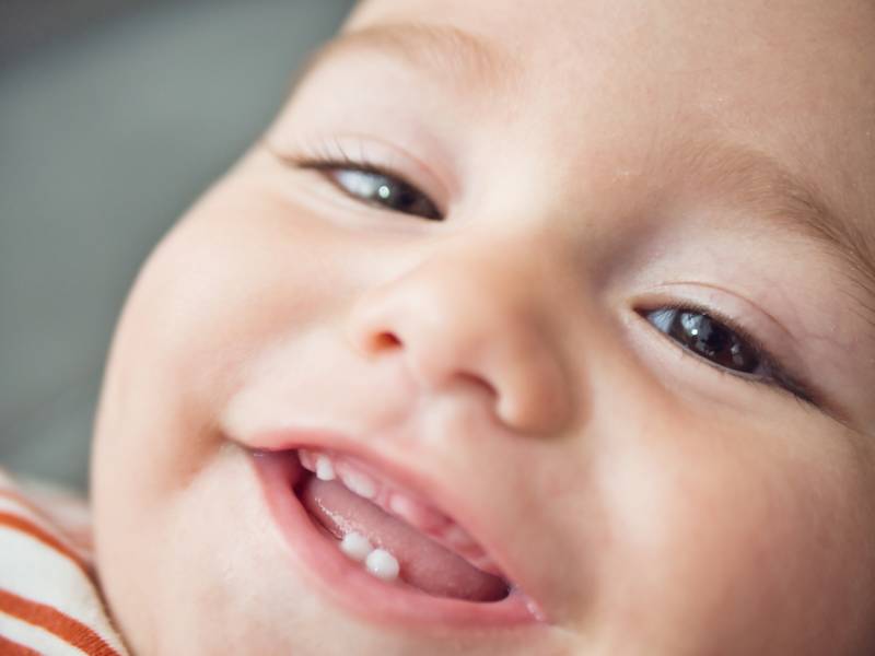 Baby’s smiling face showing new teeth, representing the special moment of the first tooth.