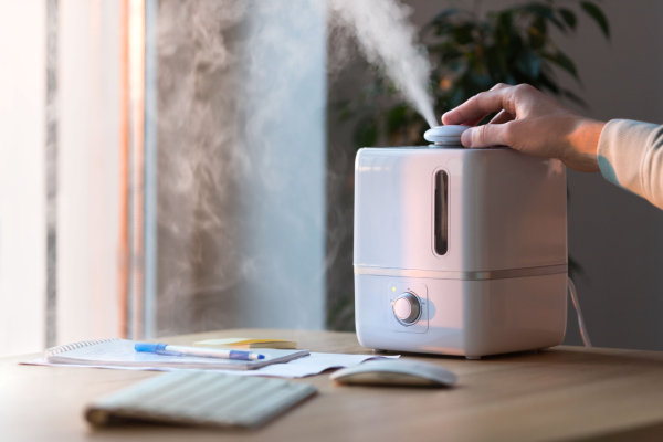 Person using an indoor humidifier to maintain air moisture and reduce skin dryness in cold weather.