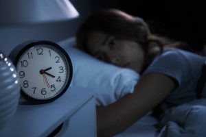 Young girl awake at night next to an alarm clock, illustrating struggles with insomnia.