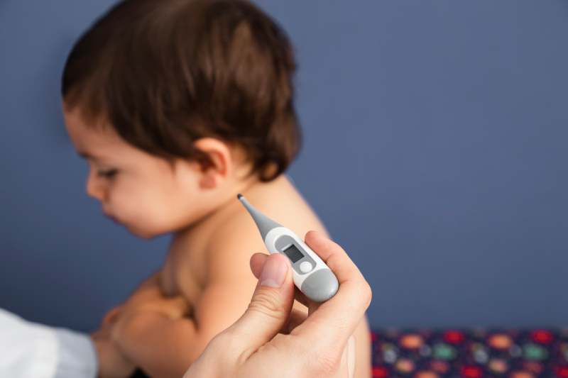Baby being checked with a thermometer, illustrating signs of common childhood illnesses.
