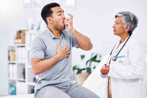 A man using an inhaler while consulting a doctor for asthma treatment.