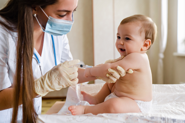 A smiling baby receiving a vaccine from a pediatrician, illustrating the importance of timely immunization.