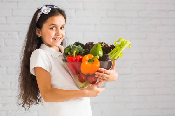 A young girl with a glass jar of vegetables, representing nutritious options for a child’s diet. 