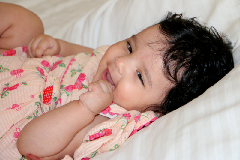 Baby lying on a bed and smiling, reflecting healthy emotional and developmental growth.