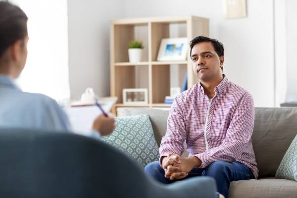 Woman psychologist observing a male patient on a couch, representing a talk therapy session