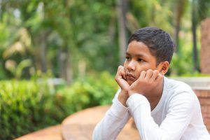 Thoughtful young boy sitting outdoors, chin on hands, suggesting signs of mental health struggles.