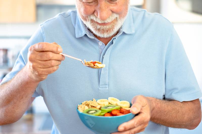The image shows an elderly man enjoying a nutritious bowl, emphasizing proper nutrition for seniors' health.