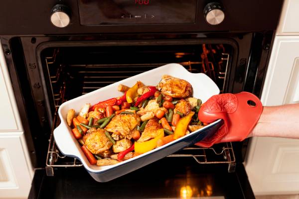 A person with an oven glove takes a dish from the oven, offering a great way to save time and money by reheating leftovers.