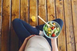 Pregnant woman eating a healthy salad, amid confusion on what foods are truly safe and recommended.