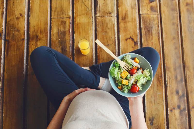 Pregnant woman eating a healthy salad, amid confusion on what foods are truly safe and recommended.