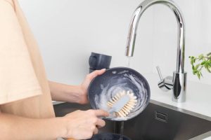 A person washes a soapy dish with a Scrub brush, using the right tool for effective cleaning.