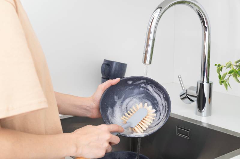 A person washes a soapy dish with a Scrub brush, using the right tool for effective cleaning.