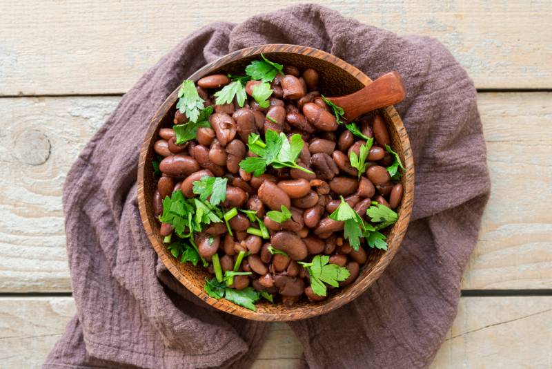 A wooden bowl filled with kidney beans topped with fresh parsley, showcasing a nutritious dish.