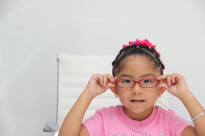 A young girl adjusting her glasses, suggesting common causes of eye problems in children.